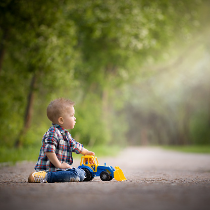 The kid plays with a bright colored tractor on the track in the park. Early development. Child playing outdoors. Lifestyle.