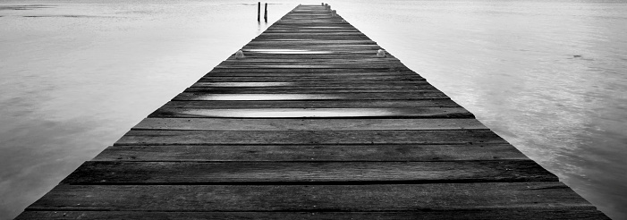 Dawn on a wooden jetty stretching into the silent ocean in stunning black and white
