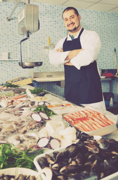 istock Seller in black apron showing fish on his counter 1158498698