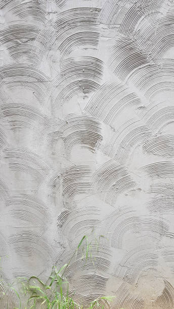 istock Textured patterned cement wall plastering with circle scratches. Grunge textures of rough cement wall surface and green plants growing in bottom side of building wall. Abstract background. 1158498727