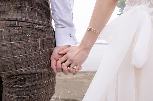 Close-up of bride and groom holding hands on beach