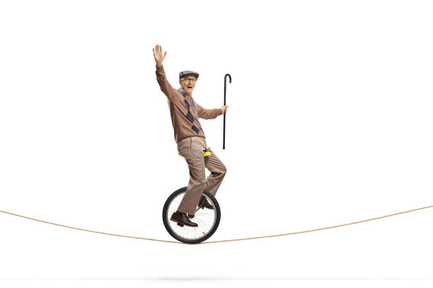 istock Elderly man riding a unicycle on a rope and holding a walking cane 1158508033