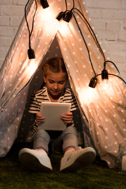 istock Smiling kid sitting in cozy wigwam and holding digital tablet 1158510469