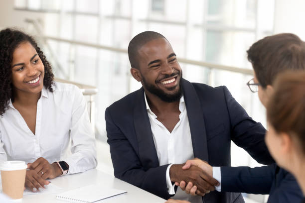 Smiling black businessman handshake male partner at meeting Smiling african American businessman in suit handshake male colleague get acquainted at office meeting, excited black man employee shake hand greeting with business partner a briefing professional thank you stock pictures, royalty-free photos & images