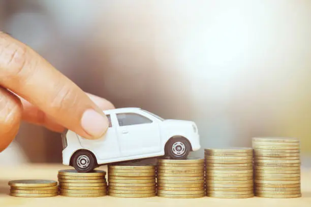 Business man and close up hand holding model of toy car on over a lot money of stacked coins - insurance, loan and buying car finance concept. buy and installments down payment a car.