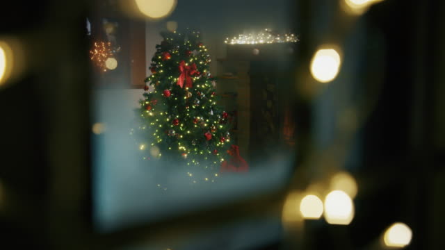 Slow motion of cozy living room with fireplace, lights and decorated Christmas tree viewed from snowy window.