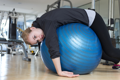 Joven mujer caucásica tumbada en la bola gimnástica azul mirando exhausta, cansada, aburrida y cansada en el gimnasio photo