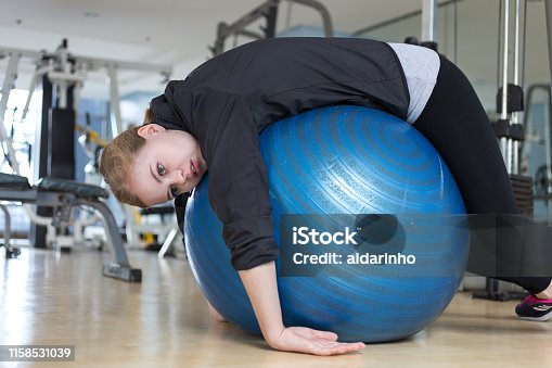 istock Young caucasian woman lying on blue gymnastic ball looking exhausted, tired, bored and weary at the gym 1158531039
