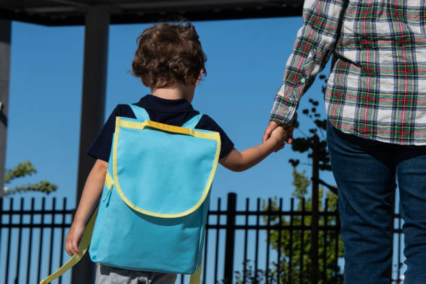 Back to school, little boy child walking to his first day of school with his mom Back to school, caucasian little boy child walking to his first day of school carrying a backpack holding his mom hand from behind nervous holding hands stock pictures, royalty-free photos & images