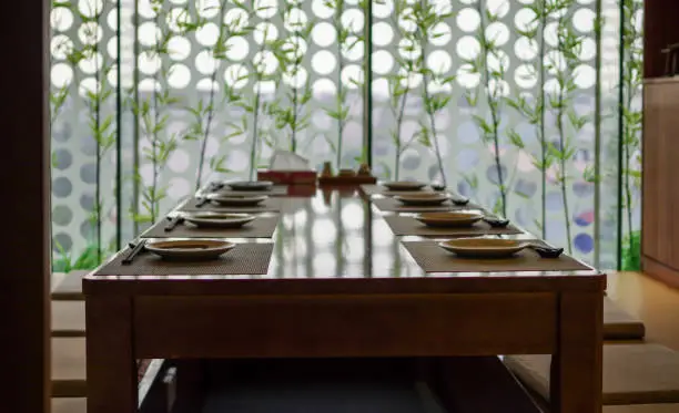 Empty japanese cuisine restaurant tatami table setting with chopsticks and plates and bamboo near window as decoration