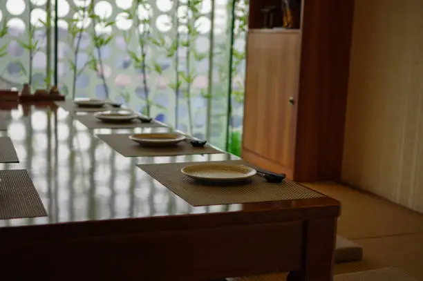 Empty japanese cuisine restaurant tatami table setting with chopsticks and plates and bamboo near window as decoration