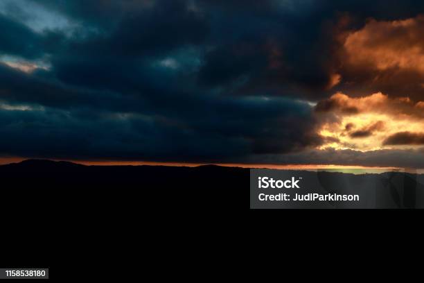 Cloudy Rural Sunset With Hills And Trees Silhouetted Stock Photo - Download Image Now