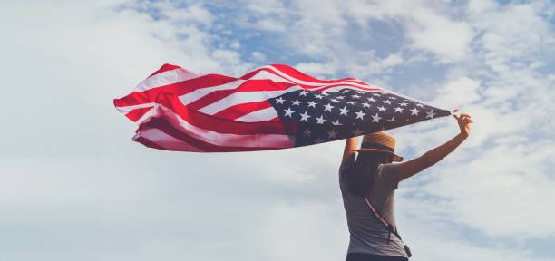 young woman holding american flag on blue sky background with copy space.vintage tone.concept of america celebrate 4th of july. - american flag flag usa sky imagens e fotografias de stock