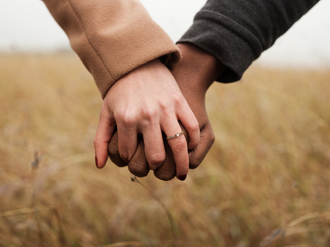 A close up of an engaged couple holding hands with the engagement ring on as they stand outdoors.