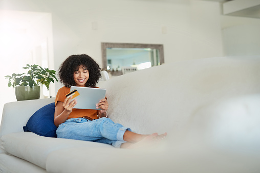 Shot of a young woman using a digital tablet and credit card while relaxing at home