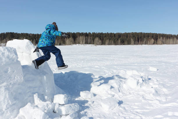 istock Boy jumping from an unfinished igloo in the snow in winter 1158547136