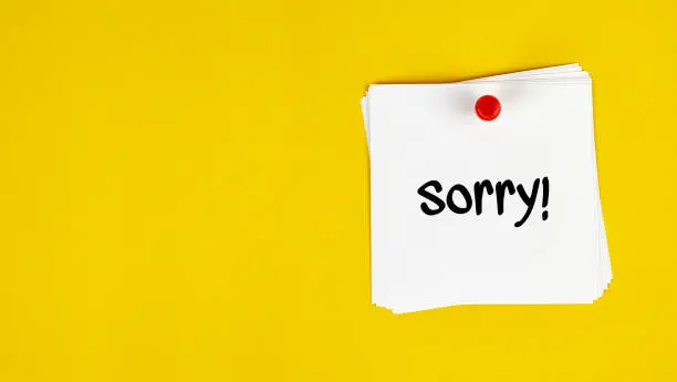 White Sticky Note With Sorry Message And Red Push Pin On Yellow Background