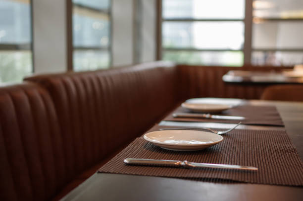 istock Plates, forks and knifes on restaurant table mat with leather sofa near window in daylight 1158554774