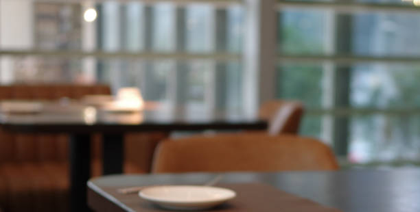 Defocused restaurant table with white plate and leather chair near window wall daylight