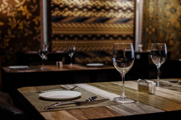 istock Empty wine glasses with white plate, knife and fork on wooden table in restaurant with silk rugs on the wall 1158557321