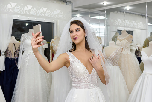 Young bride making selfie in wedding dress in salon