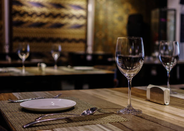 istock Empty wine glasses with white plate, knife and fork on wooden table in restaurant with silk rugs on the wall 1158557920