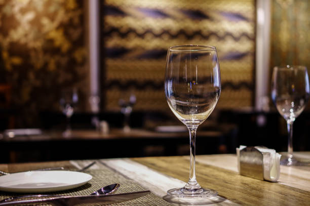 istock Empty wine glasses with white plate, knife and fork on wooden table in restaurant with silk rugs on the wall 1158557969