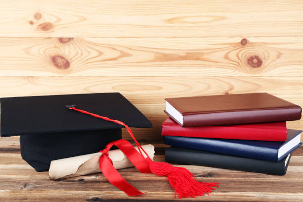 istock Graduation cap with diploma and stack of books on brown wooden table 1158558721