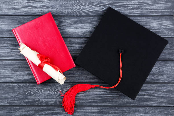 istock Graduation cap with diploma and notepad on black wooden table 1158558738
