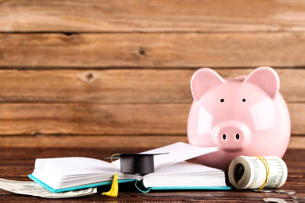 istock Piggybank with dollar banknotes, graduation cap and notepad on brown background 1158559033