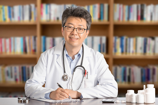 Asian male doctor sitting at desk smiling.