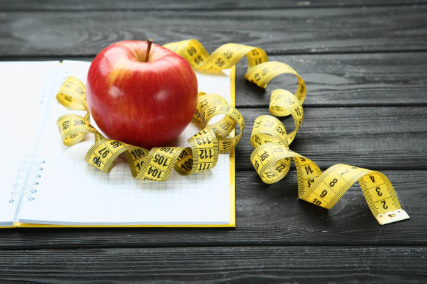 istock Measuring tape with red apple and notepad on wooden table 1158563207