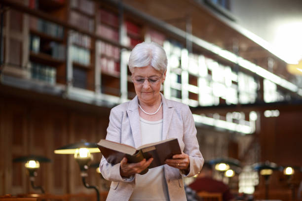 istock Senior woman reading an old book in the library 1158570174