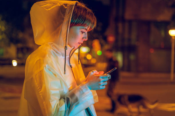 Cool young girl using phone at night under colorful light stock photo