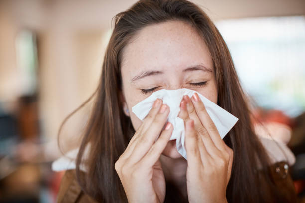 Young woman with cold or flu blows her nose on a tissue stock photo