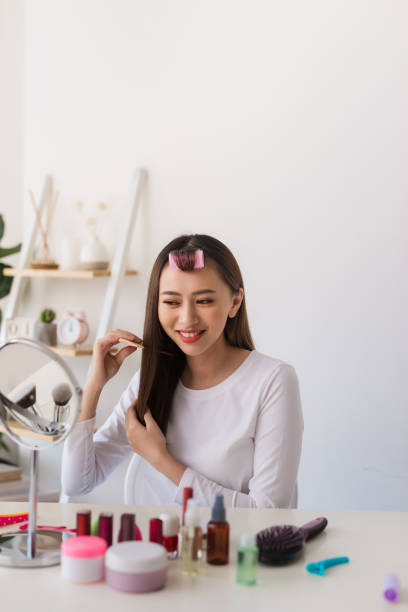 istock Hairstyle tutorial. Asian woman brushing her hair and smiling pleasantly while filming a tutorial for her beauty blog 1158574301