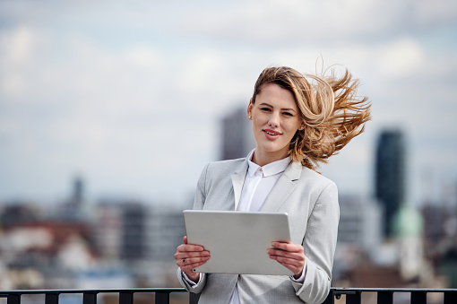 A front view of young businesswoman with tablet standing on a terrace, looking at camera.