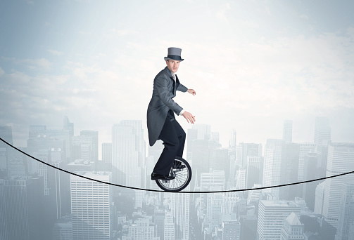 Brave guy riding a monocycle on a rope above cityscape concept