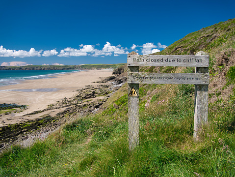 Weathered wooden sign showing a closure of the Pembrokeshire Coast Path near Newgale Beach, taken in summer against a blue sky