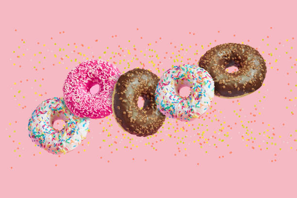 istock glazed doughnuts in motion falling on pink background with colorful sprinkles 1158583088