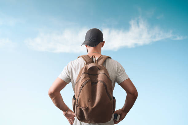 A man with a backpack is standing. View from the back. Blue sky in the background A man with a backpack is standing. View from the back. Blue sky in the background. back to front stock pictures, royalty-free photos & images