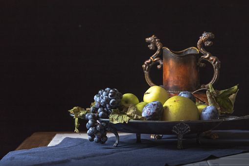 Fruit pot with apples and grapes on a old table with blue table cloths, close up