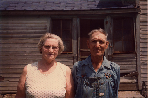 Old farmer and his wife in front of ramshackle house. Real life American Gothic. Scanned film taken in the 1970s.