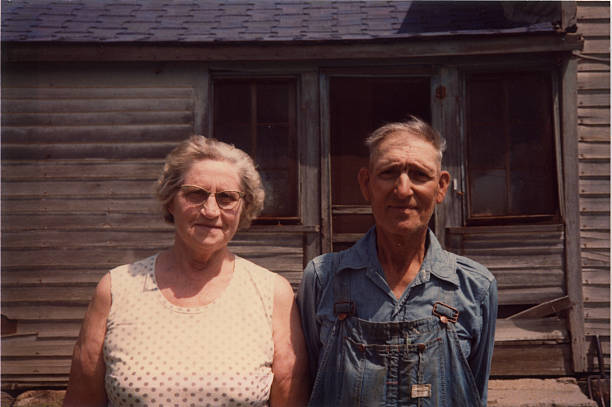 old farmer and his wife, retro Old farmer and his wife in front of ramshackle house. Real life American Gothic. Scanned film taken in the 1970s. small town america photos stock pictures, royalty-free photos & images