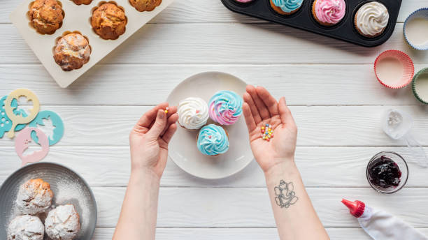 Cropped of woman holding sprinkles while decorating cupcakes on white table