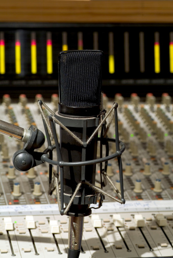 Close up of microphone over a studio control board with illuminated meters showing in background.