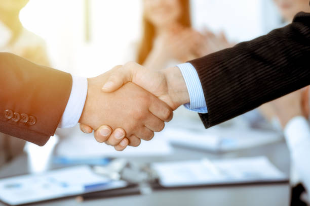 istock Business people shaking hands at meeting while theirs colleagues clapping and applausing. Group of unknown businessmen and women in modern white office. Success teamwork, partnership and handshake concept. 1158602761