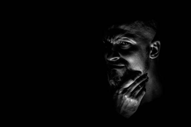 istock Face with a bearded man grimace against a dark background with sharp shadows. Comedic, fabulous villain or negative character conception with copy space. 1158604061