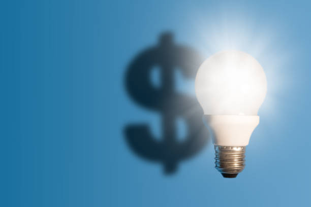 istock Light bulb on bright blue background with a dollar sign shadow. Conception good idea it's money. 1158605373