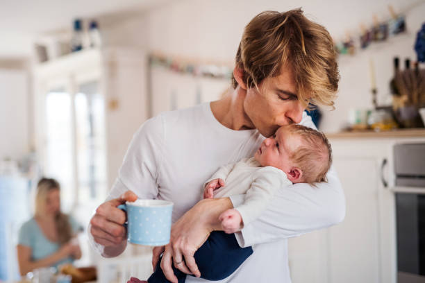 young father holding a newborn baby in kitchen at home, kissing. - mother baby new kissing imagens e fotografias de stock